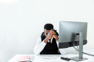 A man sits with his head in his hands at his computer as he questions his parental insurance. Many young adults feel this way when they lose their parental insurance and aren't sure what to do.